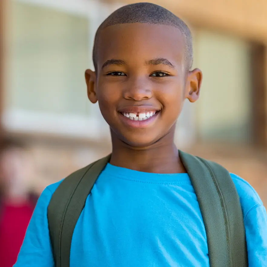 Young boy in blue shirt smiling outside of his classroom