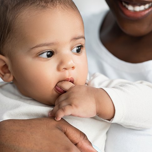 Mother holding her baby while it chews on its finger